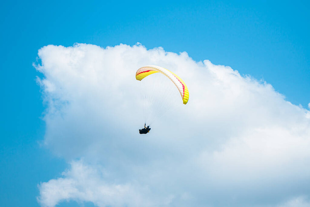 アドレナリンポンピングの極端なスポーツ, 明確な青空にパラグライダー. 晴れた日の青空と白い雲の背景を持つ空の上空のパラシュートで飛ぶパラグライダー. - 写真・画像