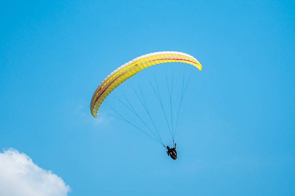 Un sport extrême adrénaline-pompage, parapente contre le ciel bleu clair. Parapente volant avec son parachute au-dessus du ciel avec un fond de ciel bleu et de nuages blancs par une journée ensoleillée. - Photo, image