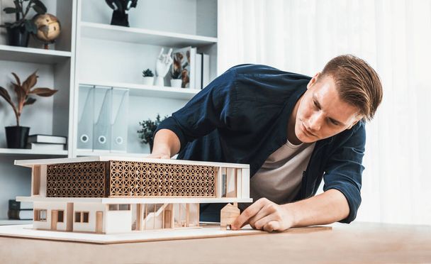 Архітектор-дизайнер вивчає елегантну модель будинку, переглядаючи дизайн споруди для поліпшення з планом будівництва на столі. Творчість та інновації в архітектурному дизайні. Ітерація - Фото, зображення