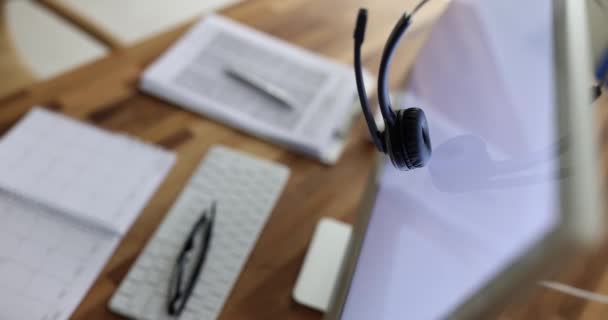 Kopfhörer mit Mikrofon hängen auf dem Computermonitor am Arbeitsplatz des Bedieners Nahaufnahme 4k-Film. Helpdesk-Konzept - Filmmaterial, Video
