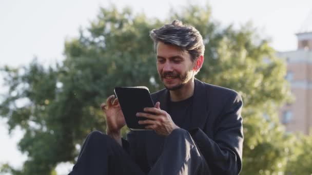 Mladík si prohlíží tablet v parku. Spokojen dospělý muž pomocí tabletu posílání zpráv přítelkyně. Úspěšný podnikatel zkontroluje svou internetovou peněženku a zkontroluje kryptografickou rovnováhu. Vysoce kvalitní 4K záběry - Záběry, video