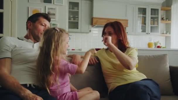 A happy american dream family is playing rock paper scissors in the room on the sofa. Mother won and laugh with daughter merrily. Father tickles her. Pleasant good nostalgia for childrens games. High - Footage, Video