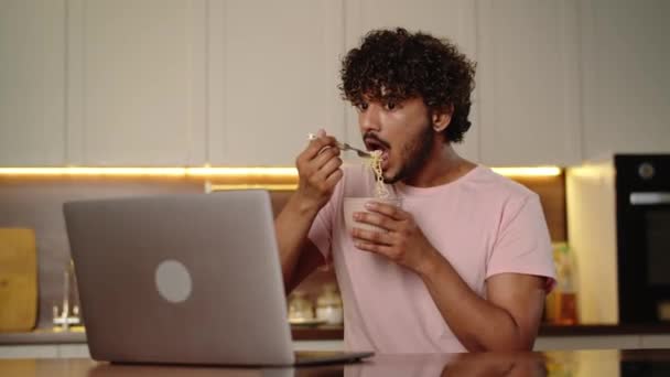 Un jeune homme qui mange de la soupe ramen à la maison. Homme drôle tenant bol nouilles instantanées et regarder la vidéo sur ordinateur. Homme appréciant sa nourriture détendue voir série. Dîner tard dans la nuit. Haut - Séquence, vidéo