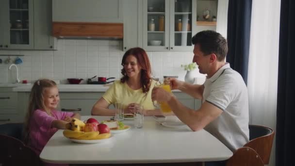 Positiivinen amerikkalainen unelma perhe keittiössä syödä aamiaista tai lounasta. Hymyilevä äiti, isä ja tytär syövät ja keskustelevat mukavasti. Onnellisen lapsuuden ja vanhemmuuden käsite. Laadukas 4k - Materiaali, video