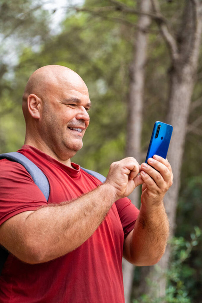 Portré, mosolygós férfi használja az okostelefont az erdőben - Fotó, kép