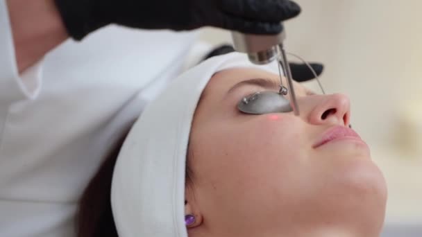 Крупный план женщины, проходящей антивозрастную процедуру для лица с помощью лазера YAG в салоне красоты. Аппаратная косметология - Кадры, видео