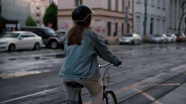 Vista trasera de la joven en casco protector montando una bicicleta para trabajar en la ciudad. Señora disfrutando de su viaje ecológico a la oficina - Metraje, vídeo