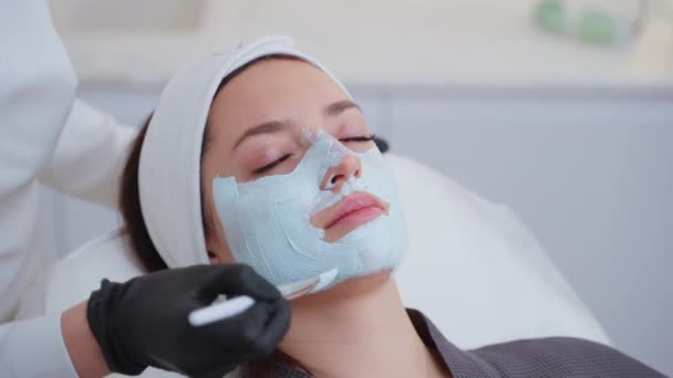 Zbliżenie kobiety korzystającej z leczenia twarzy z glinianą maską w salonie piękności. Kosmetologia i spa - Materiał filmowy, wideo