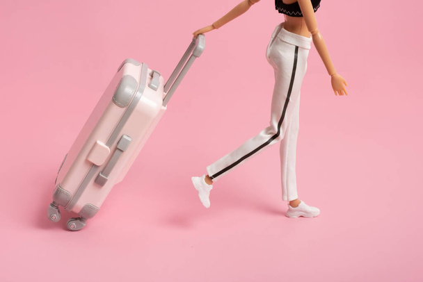 The doll carries a suitcase on wheels. Travel, vacation creative minimalistic concept. - Photo, Image