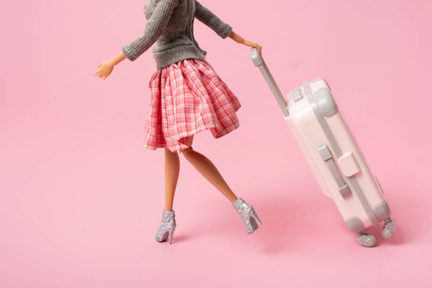 A boneca carrega uma bagagem sobre rodas. Viagem, férias conceito minimalista criativo. - Foto, Imagem