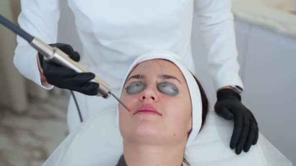 Mujer teniendo sesión de salón de belleza. Cosmetólogo que proporciona terapia de piel facial con láser YAG. Tratamiento anti-envejecimiento - Imágenes, Vídeo