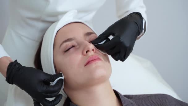 Fotografia de perto de um cosmetologista usando almofadas de algodão para remover o produto cosmético do rosto feminino após o procedimento de limpeza da pele. Tratamento facial no salão de beleza - Filmagem, Vídeo
