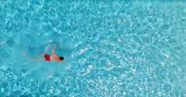 Widok z góry na mężczyznę w czerwonych spodenkach pływającego w basenie. Letni styl życia. Zwolniony ruch - Materiał filmowy, wideo