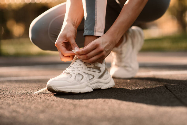 An athlete ties a white sneaker in a close-up on a sports field. Fintes in the open air - Photo, Image