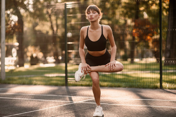 A young, athletic woman is exercising on the sports field. The concept of weight loss. Beautiful figure. Fintes exercises. Training in the open air. High quality photo - Photo, Image