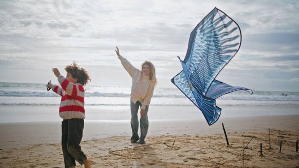 Mother son launching kite on windy ocean shore. Cheerful woman helping child with toy on autumn weekend. Excited little boy playing rest beach with babysitter. Supportive loving family relationships - Photo, Image