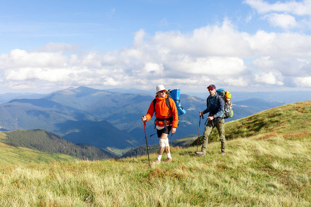 два чоловіки з пішохідним обладнанням і рюкзаками йдуть в гори з пішохідними стовпами на тлі ландшафту, туристи в окулярах піднімаються в гори разом - Фото, зображення
