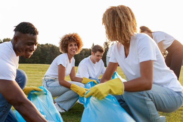 πολυφυλετική ομάδα εθελοντών με σακούλες σκουπιδιών συλλέγουν σκουπίδια και πλαστικά στο πάρκο, ομάδα μαθητών καθαρό περιβάλλον, έννοια πράσινου πλανήτη και πλαστική απαγόρευση - Φωτογραφία, εικόνα