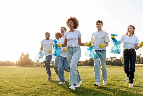 multiraciale groep van mensen die rennen om het park schoon te maken van afval en plastic met handschoenen en vuilniszakken, team van vrijwilligers verheugen zich en buiten te vieren, milieuzorg concept - Foto, afbeelding