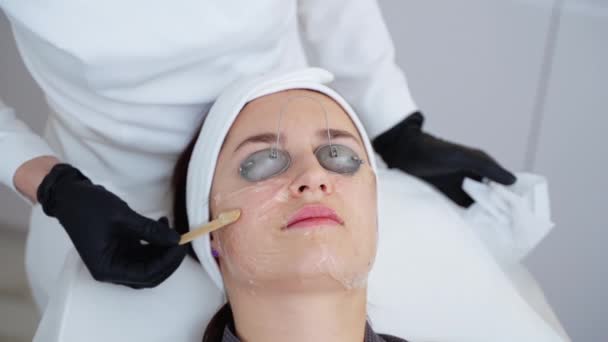 Крупный план подготовки кожи лица к широкополосному лазерному лечению. Косметолог наносит охлаждающий гель, женские глаза защищены - Кадры, видео