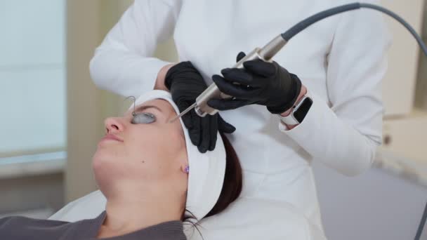 Женщина в салоне красоты. Она проходит лечение лица профессиональным косметологическим оборудованием. Лечение кожи с помощью лазера YAG - Кадры, видео