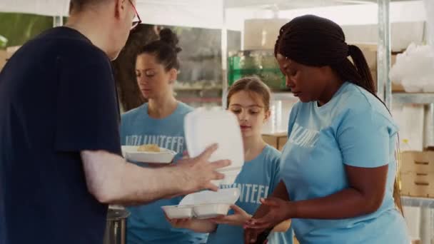 Vrouwelijke vrijwilligers van verschillende etniciteiten voorzien daklozen van vers fruit en gratis maaltijden. Vrijwilligerswerk op voedsel rijden, Kaukasische en Afrikaanse Amerikaanse dames helpen de behoeftige en minder fortuinlijke. - Video