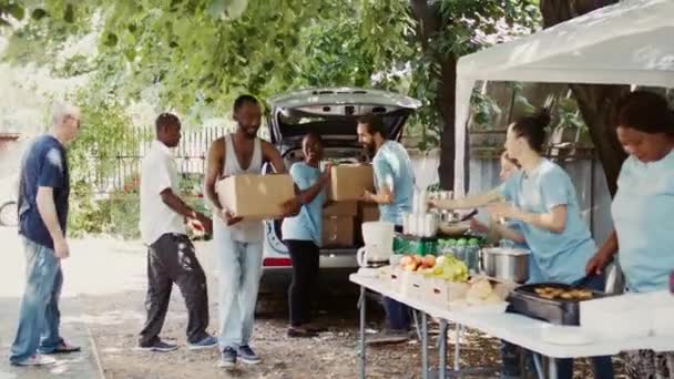 Door toegewijde vrijwilligers worden behoeftige mensen voorzien van maaltijddozen en conserven. Glimlachende liefdadigheidswerkers die de voedselindustrie vertegenwoordigen en non-profit organisatie voeden de daklozen. - Video