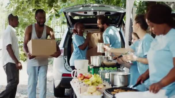 Çok ırklı gönüllülerden oluşan bir grup ihtiyaç sahiplerine yiyecek kutuları ve konserveleri dağıtıyor. Gönüllü bireyler fakir ve evsiz insanlara insani yardım sunuyor. Üçayak atışı. - Video, Çekim