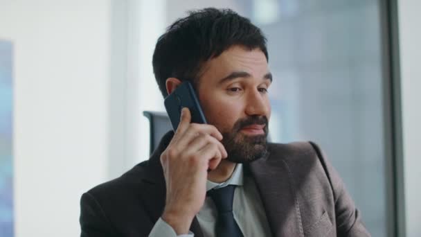 Zakenman geniet van een vriendelijk telefoongesprek op kantoor van dichtbij. Gelukkige succesvolle executive manager lachen praten smartphone op de werkplek. Ontspannen bebaarde werknemer glimlachend op telefoongesprek. - Video