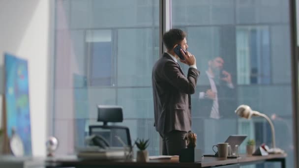 Elegant business man calling partners standing luxury office sunny morning. Confident bearded man entrepreneur talking cell phone writing notes at work desk. Busy ceo making appointment by telephone. - Footage, Video