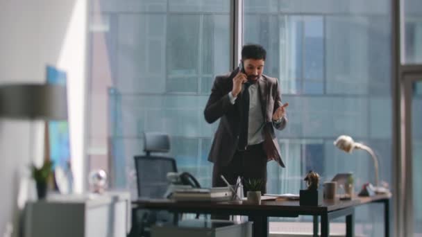 Employee frustrated by phone call standing office looking business documents. Angry bearded businessman arguing on telephone conversation at workplace. Stressed manager speaking smartphone nervously. - Footage, Video
