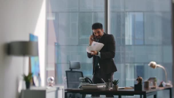 Excited broker laughing calling phone standing modern office. Emotional businessman throwing papers up rejoicing great deal sharing good news by telephone. Happy ceo feeling success talking cellphone. - Footage, Video