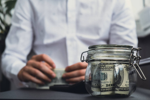 Dollar Banknote Saving Money In Glass Jar. Unrecognizable man calculate money on calculator Moderate Consumption And Economy Collecting Money Tips Business Finance concept - Photo, Image