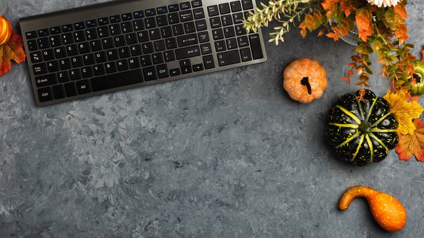 Laptop na biurku z żółtymi liśćmi i dyniami na ciemnoszarym tle. Płaski, widok z góry z jesiennym wystrojem - Zdjęcie, obraz