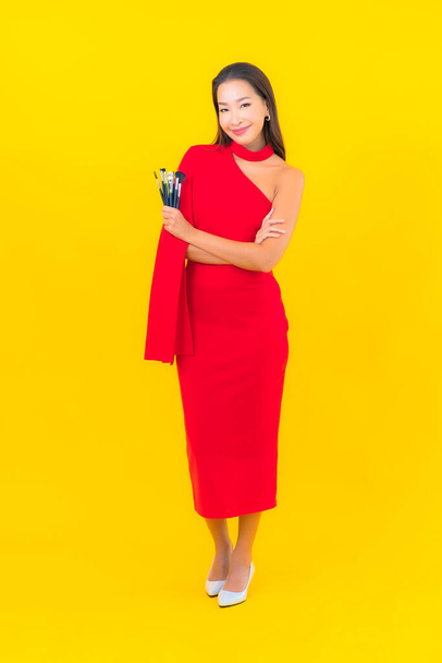 Porträt schöne junge asiatische Frau mit Make-up Pinsel auf gelbem Hintergrund - Foto, Bild