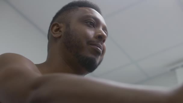 Az afro-amerikai férfi pedálozza az orbitreket a kardiológiai szobában a funkcionális rehabilitáció alatt. Szív- vagy érrendszeri betegségben szenvedő felnőtt beteg. Elektrokardiográfia a modern klinikán vagy kórházban. Portré - Felvétel, videó
