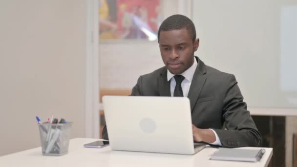 Empresario africano que trabaja en el ordenador portátil mientras está sentado en la oficina - Imágenes, Vídeo