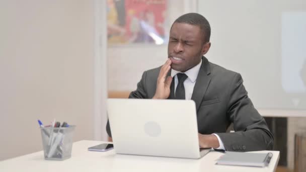 Afrikanischer Geschäftsmann mit Zahnschmerzen arbeitet im Büro am Laptop - Filmmaterial, Video