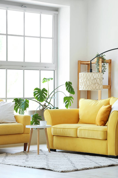 Innenraum des hellen Wohnzimmers mit gelbem Sofa und Sessel in der Nähe des großen Fensters - Foto, Bild