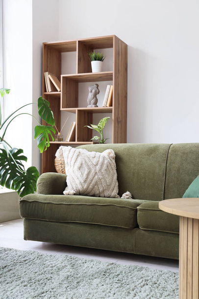 Інтер'єр світлої вітальні з затишним зеленим диваном, стелажами і кімнатними рослинами - Фото, зображення
