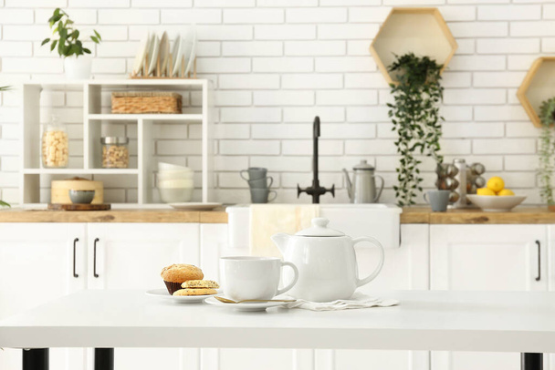 Интерьер светлой кухни с чайником, чашкой и закусками на столе - Фото, изображение