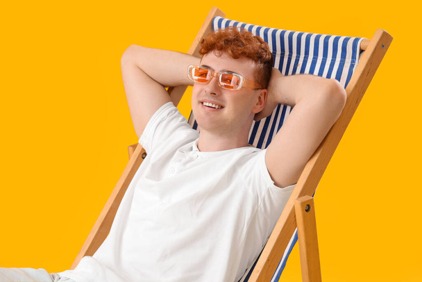 Hombre joven descansando en la silla de cubierta sobre fondo amarillo - Foto, imagen