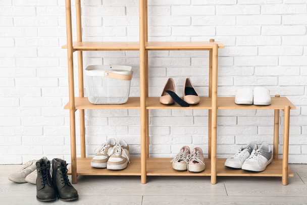 Κομψά παπούτσια και ορθοπεδική σόλα σε ξύλινο ράφι παπουτσιών κοντά σε τοίχο από ελαφρύ τούβλο - Φωτογραφία, εικόνα
