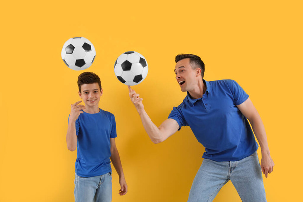 Маленький хлопчик з батьком грає у футбол на жовтому тлі - Фото, зображення