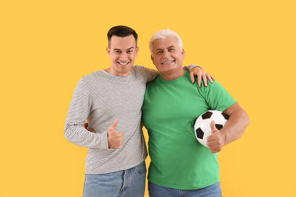 Mladý muž se svým otcem a fotbalový míč objímání na žlutém pozadí - Fotografie, Obrázek