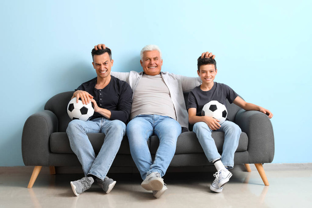 Malý chlapec se svým otcem a dědečkem drží fotbalové míče u modré zdi - Fotografie, Obrázek