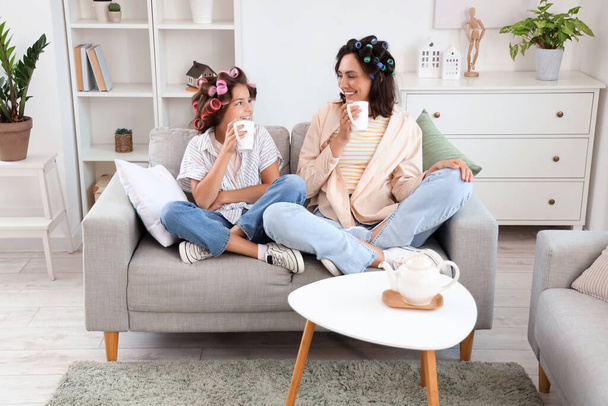 Menina e sua mãe com encrespadores de cabelo bebendo chá em casa - Foto, Imagem