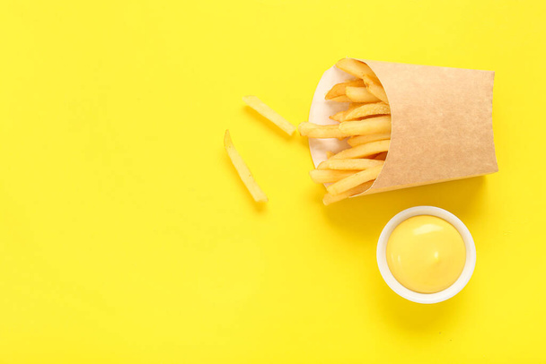 Papieren doos met heerlijke frietjes en kom mayonaise op gele achtergrond - Foto, afbeelding