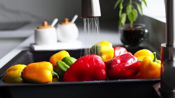 Yellow and red pepper are washed in a special tray for vegetables. The stream of water pours on the pepper in the sink. Slow motion. The interior of a modern kitchen. - Felvétel, videó