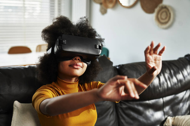 リビングルームでビデオゲームをプレイする仮想現実シミュレータを身に着けている十代の少女 - 写真・画像